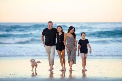 Familia feliz con sus hijos y perro paseando por la playa al atardecer, representando la armonía y las normas en la familia.