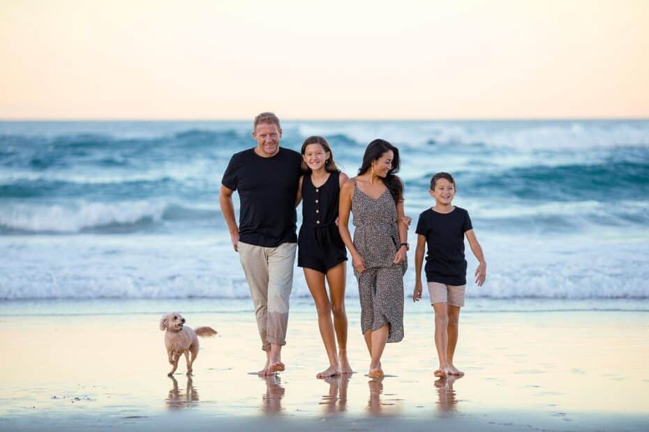 Familia feliz con sus hijos y perro paseando por la playa al atardecer, representando la armonía y las normas en la familia.